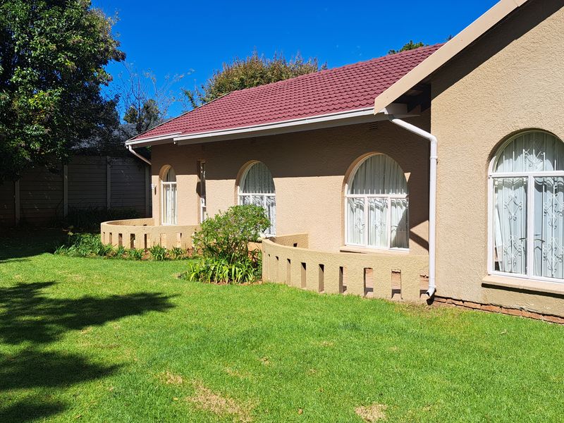 Rear view of the house featuring a tiled roof, arched windows with security bars, and low masonry garden walls set against a lawn.