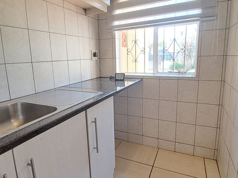A functional scullery or laundry area featuring a stainless steel double sink, granite countertops, and full-height ceramic wall tiling.