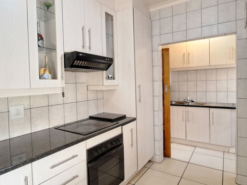 A functional kitchen featuring white cabinetry, dark granite countertops, built-in oven and hob, with an adjoining scullery area.