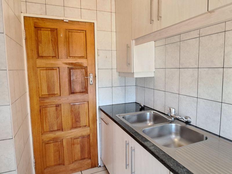 A functional scullery area featuring a double stainless steel sink, granite countertops, ample built-in cabinetry, and tiled splashbacks.
