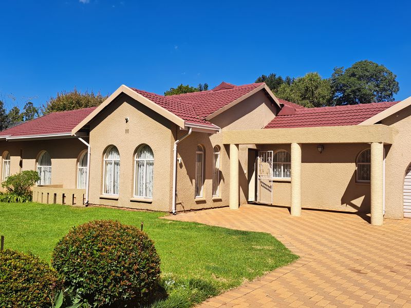 A well-maintained single-story house featuring a tiled roof, paved driveway, integrated garage, and arched windows set within a landscaped garden.