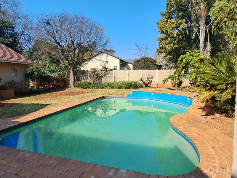 Outdoor pool area featuring a kidney-shaped swimming pool with brick paving, surrounded by a garden and perimeter walling.
