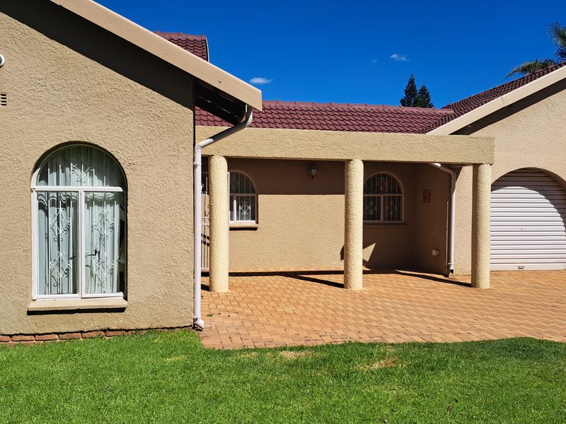 Front elevation of a residential house featuring a paved driveway, covered patio area, arched windows with security bars, and multiple garage doors.