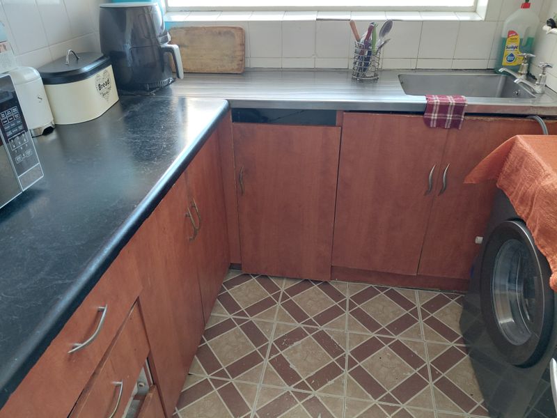 A functional kitchen featuring laminate cabinetry, a stainless steel sink, and tiled flooring, currently showing signs of wear and missing cabinet components.