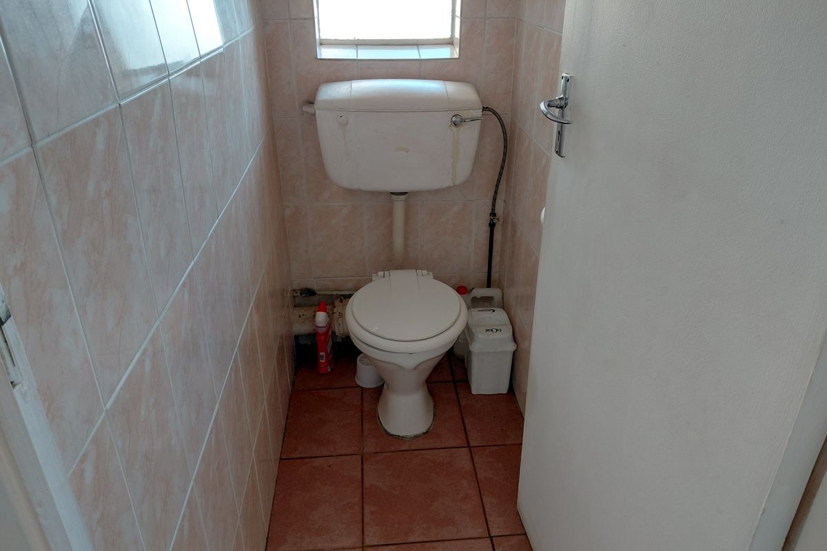 A compact, dated bathroom featuring ceramic wall and floor tiles, a standard toilet with cistern, and a small window for natural light.