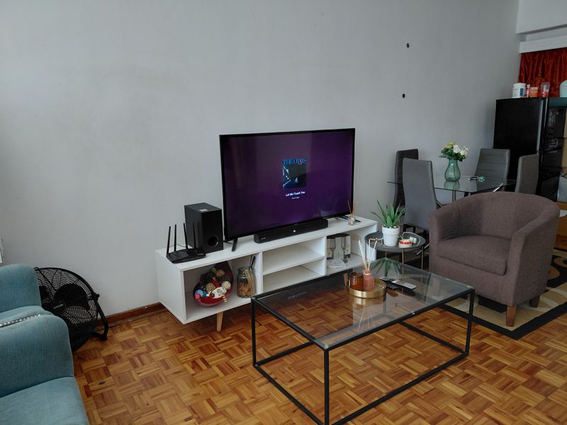 A living room area featuring classic parquet flooring and neutral wall finishes, providing a functional space for relaxation and dining.