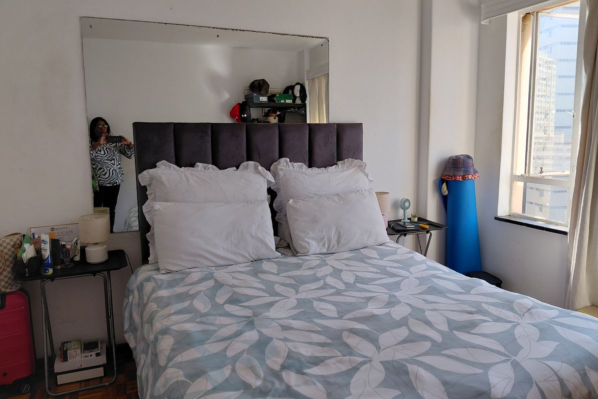 A bedroom featuring parquet flooring, a large wall-mounted mirror, and a window providing natural light.