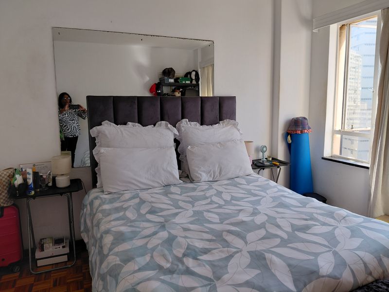 A bedroom featuring parquet flooring, a large wall-mounted mirror, and a window providing natural light.