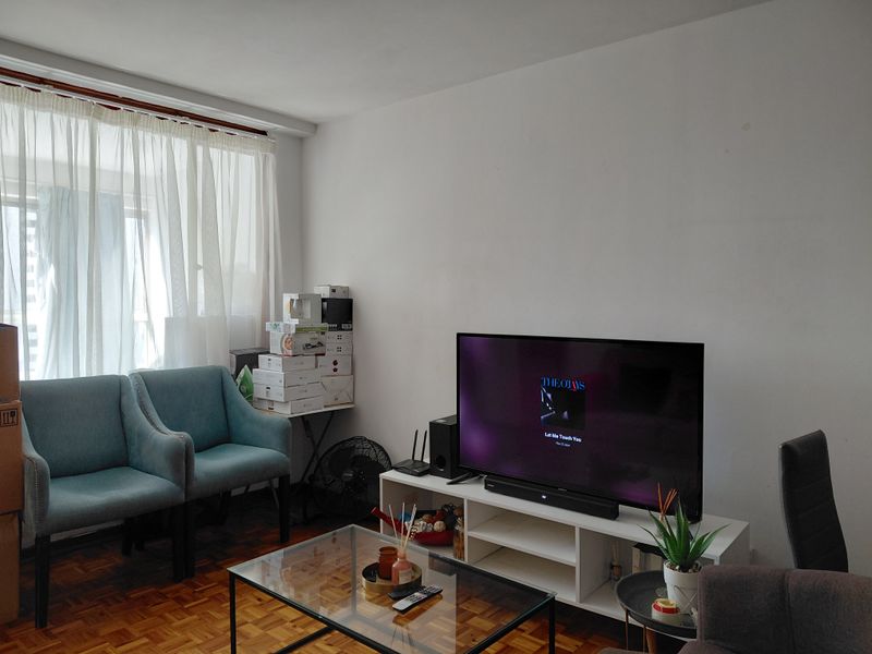 A living room featuring classic parquet flooring and natural light through a window with curtain fixtures.