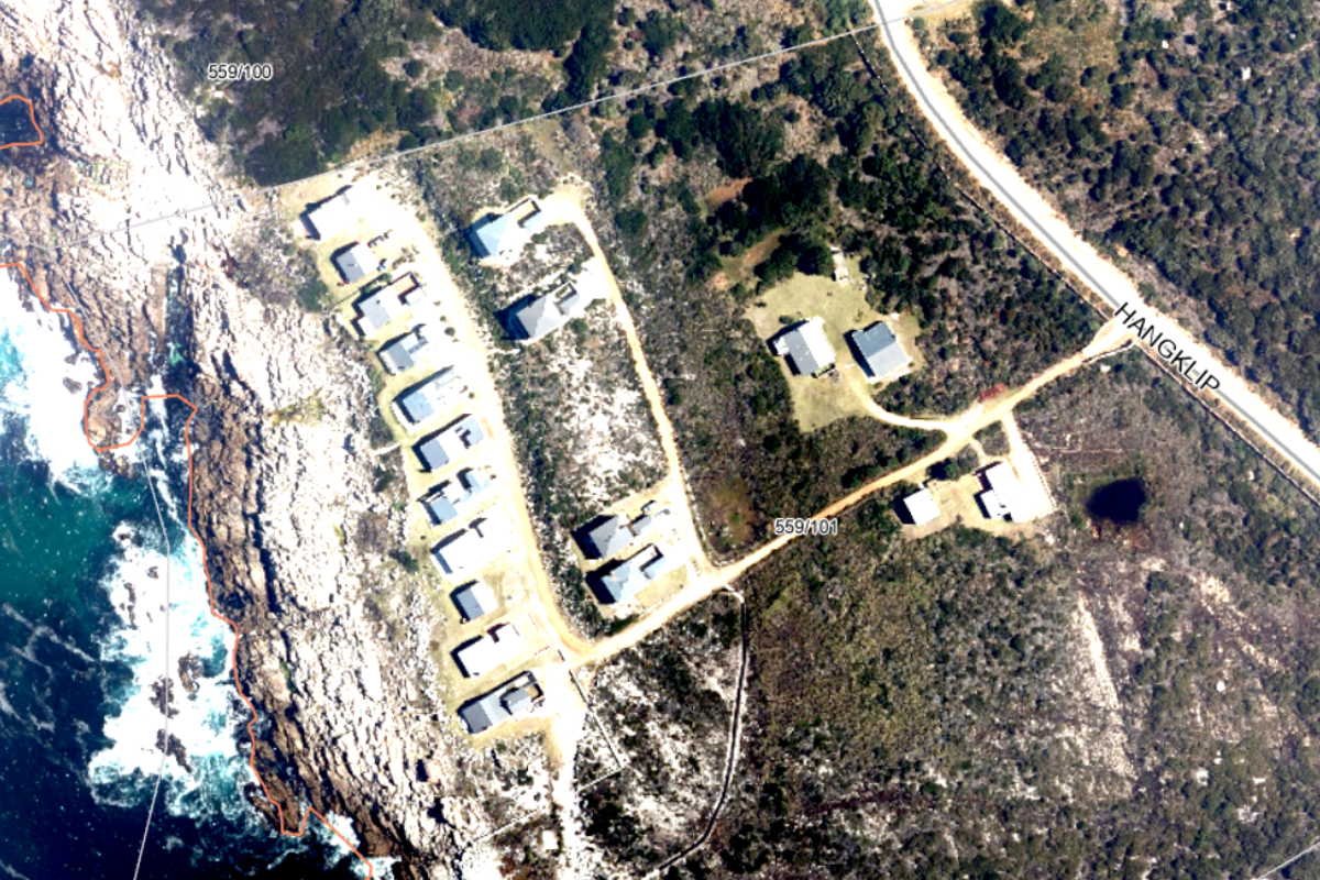An aerial view of a coastal residential area showing multiple plots, natural vegetation, and access roads near the shoreline.