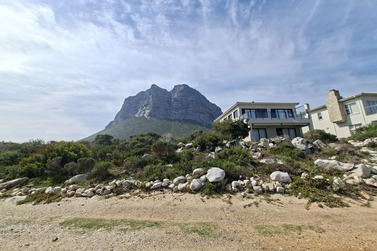 Rear view of the residential property featuring a stone retaining wall, landscaped garden, and a balcony with mountain views.