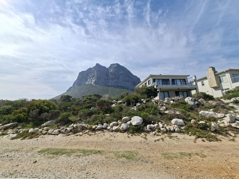Rear view of the residential property featuring a stone retaining wall, landscaped garden, and a balcony with mountain views.