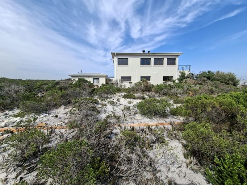 A two-story residential property situated on a sandy coastal plot with native vegetation and clear views of the building's rear elevation.