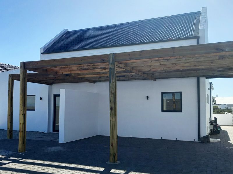 Rear view of a modern home featuring a timber pergola, paved driveway, and clean white exterior walls with a corrugated metal roof.