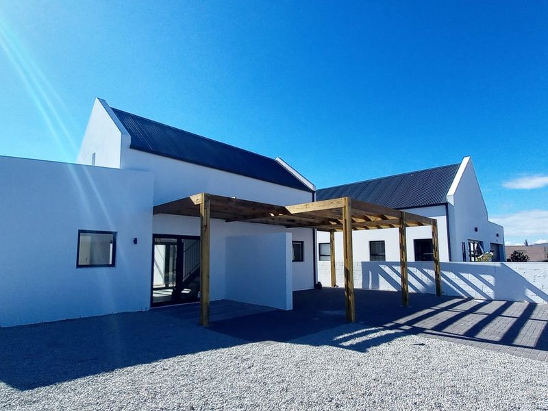 Modern architectural home exterior featuring a clean white facade, dark metal roofing, and a timber pergola over a paved entrance area.