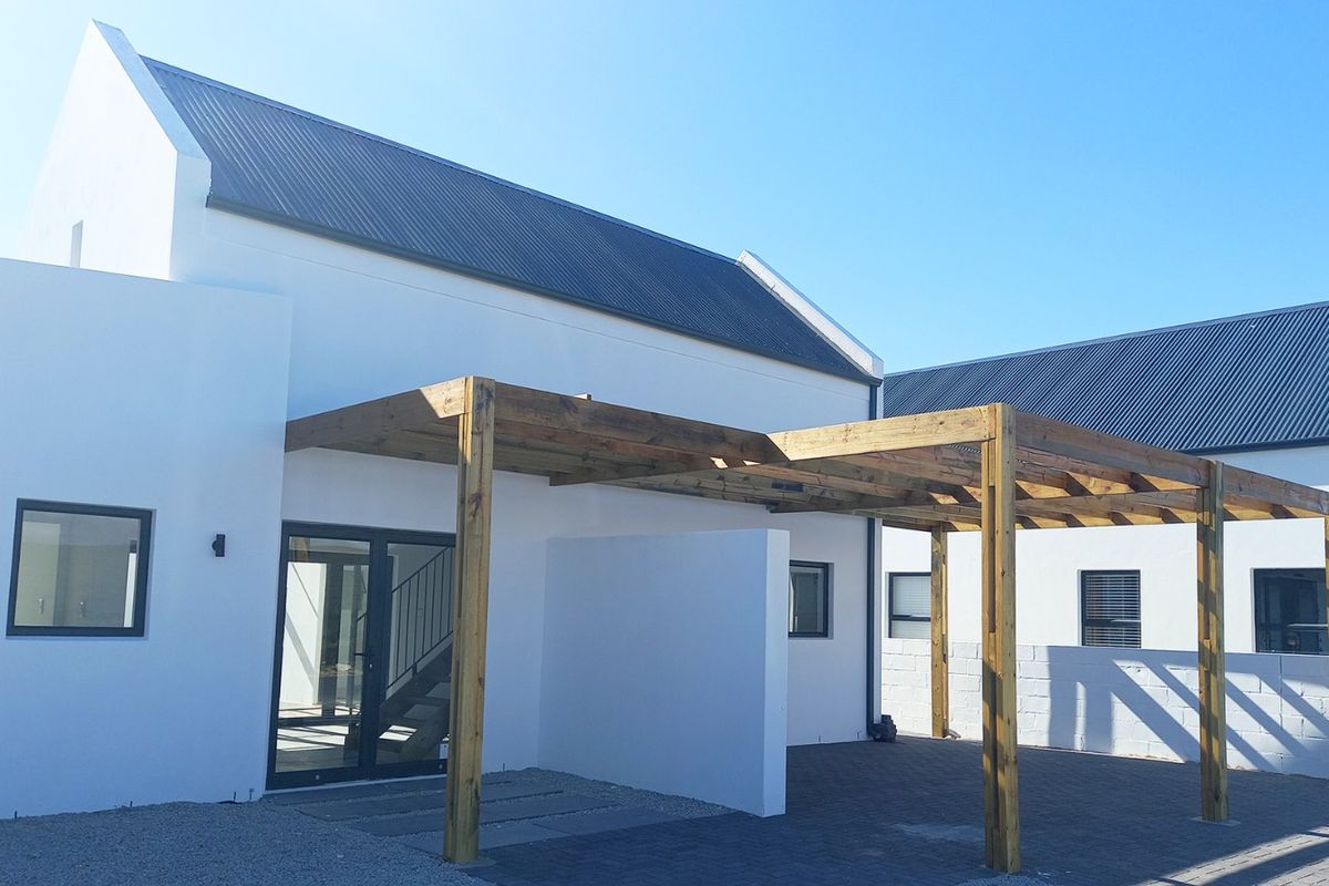 A modern rear exterior view featuring a timber pergola over a paved patio area, complemented by clean white walls and dark metal roofing.