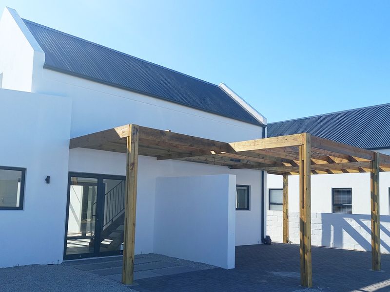 A modern rear exterior view featuring a timber pergola over a paved patio area, complemented by clean white walls and dark metal roofing.