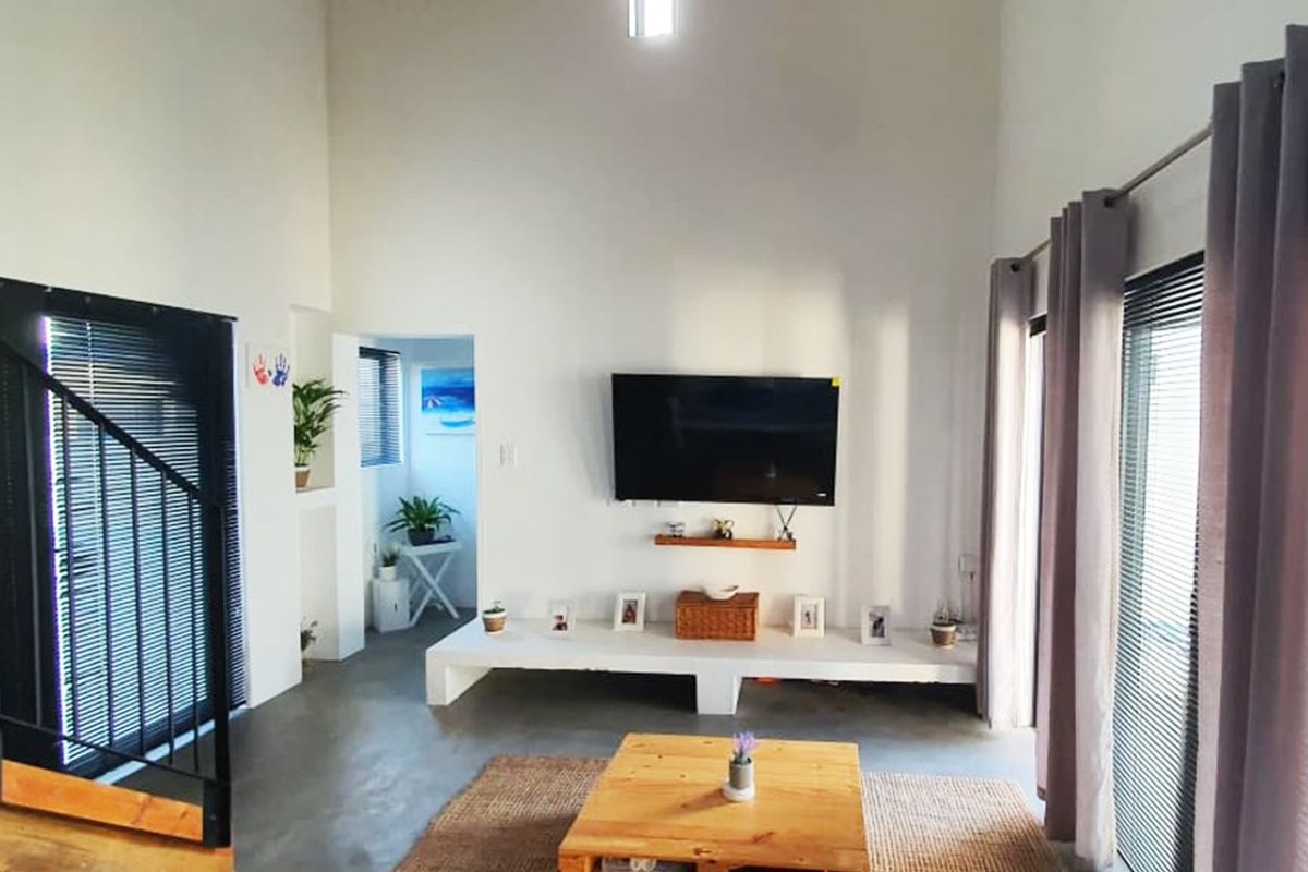 A bright living room featuring polished concrete floors, a built-in media console, and a staircase with a modern metal railing.