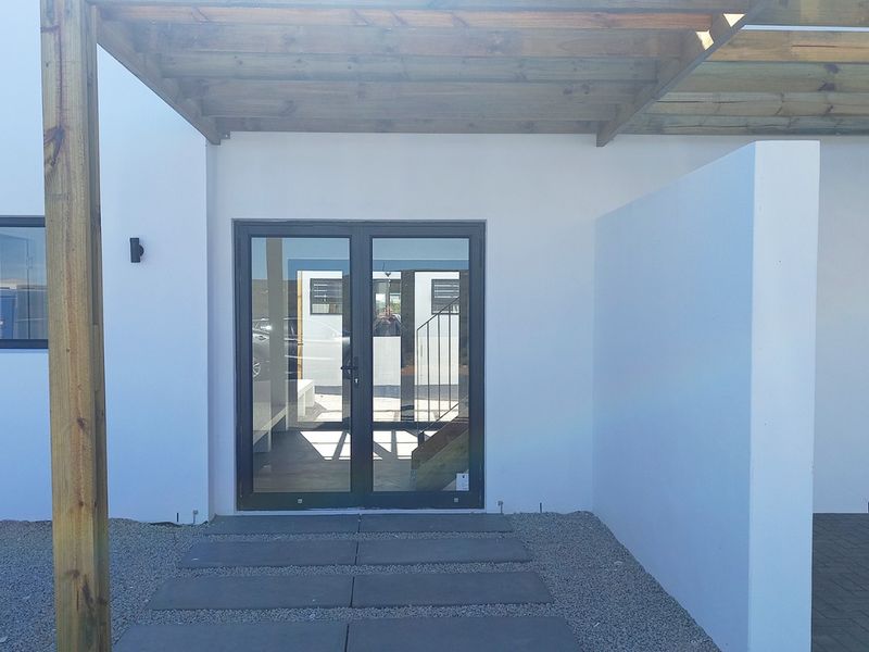 Modern front entrance featuring a timber pergola, double glass doors, and clean paved walkway with gravel landscaping.