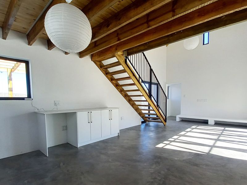 Spacious open-plan living area featuring polished concrete floors, exposed timber beams, a modern timber staircase, and large bi-fold doors leading to the outdoors.