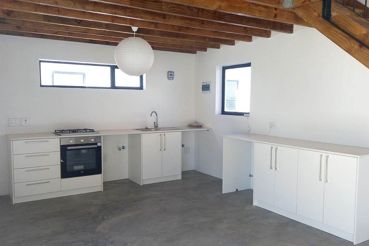 Modern kitchen featuring white cabinetry, built-in oven, gas hob, concrete flooring, and exposed timber ceiling beams, situated beneath a staircase.