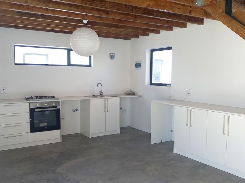 Modern kitchen featuring white cabinetry, built-in oven, gas hob, concrete flooring, and exposed timber ceiling beams, situated beneath a staircase.