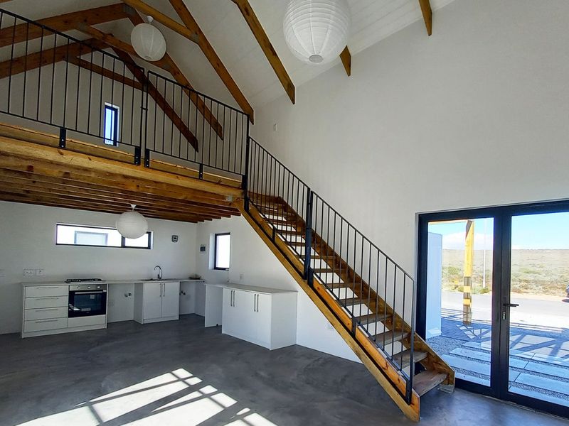 Spacious open-plan living area featuring a modern kitchen, polished concrete floors, exposed timber trusses, and a mezzanine level with a staircase.