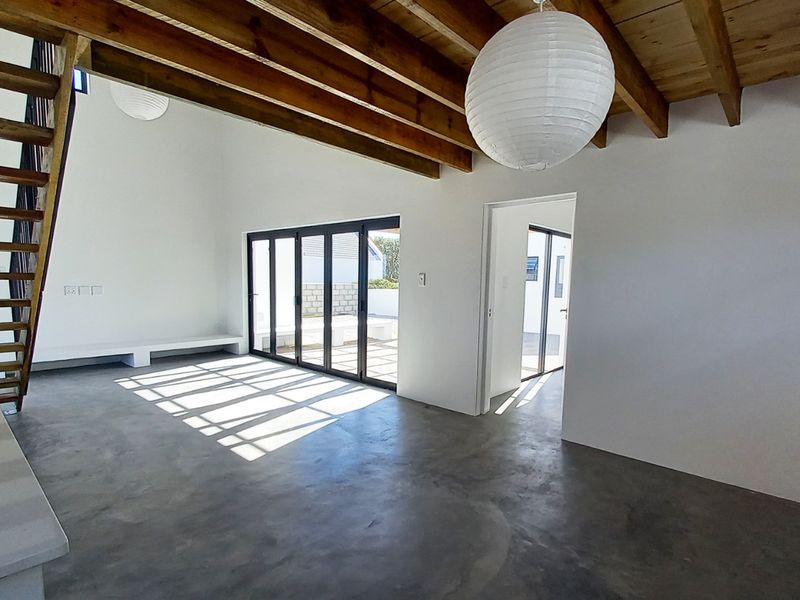 Spacious open-plan living area featuring polished concrete floors, exposed timber beams, and bi-fold doors leading to an outdoor space.