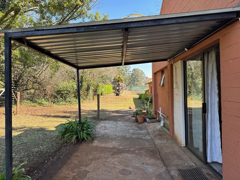 A covered outdoor patio area featuring a metal roof structure, concrete flooring, and direct access to the garden through a sliding glass door.