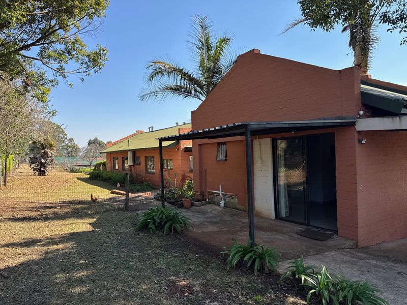 Rear view of the cottage featuring a covered patio area, sliding glass doors, and established garden space with perimeter fencing.