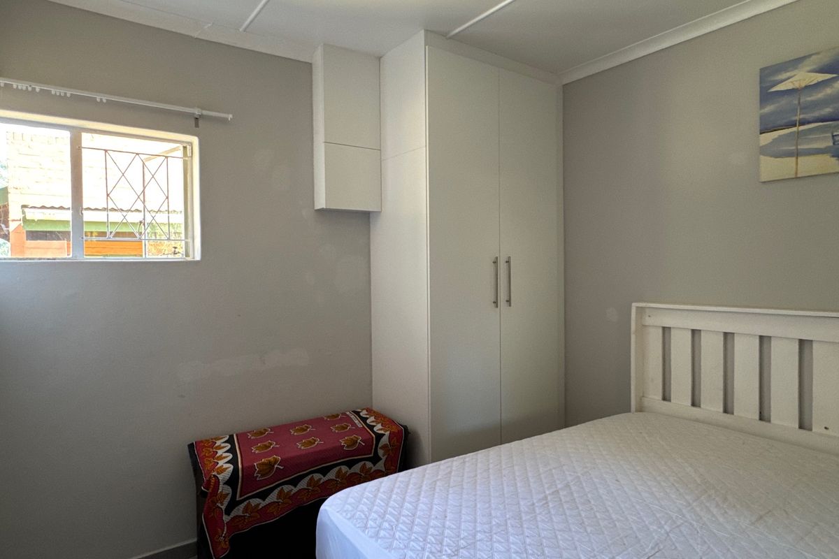 A functional bedroom featuring a built-in wardrobe, security bars on the window, and neutral wall finishes.