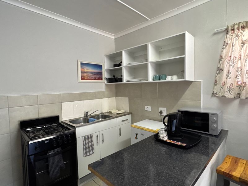 Compact kitchen featuring a gas stove, double sink, granite countertops, and ample built-in cabinetry with open shelving for storage.