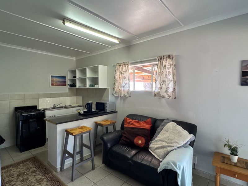 Open-plan living area featuring a compact kitchen with built-in cabinetry, a breakfast bar, and tiled flooring throughout.