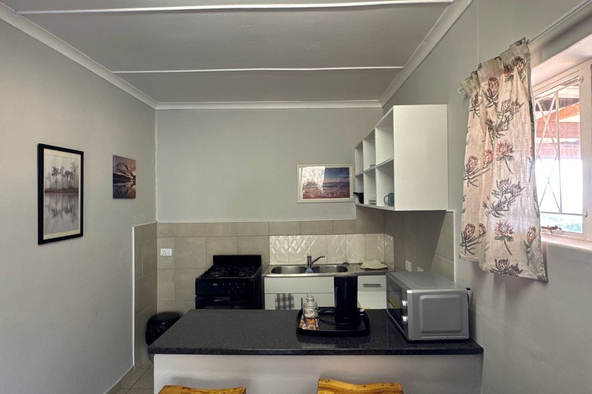 Compact kitchen featuring a breakfast bar, double sink, tiled backsplash, and built-in cabinetry with open shelving.