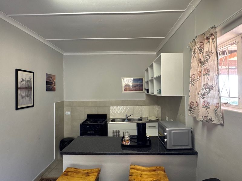 Compact kitchen featuring a breakfast bar, double sink, tiled backsplash, and built-in cabinetry with open shelving.