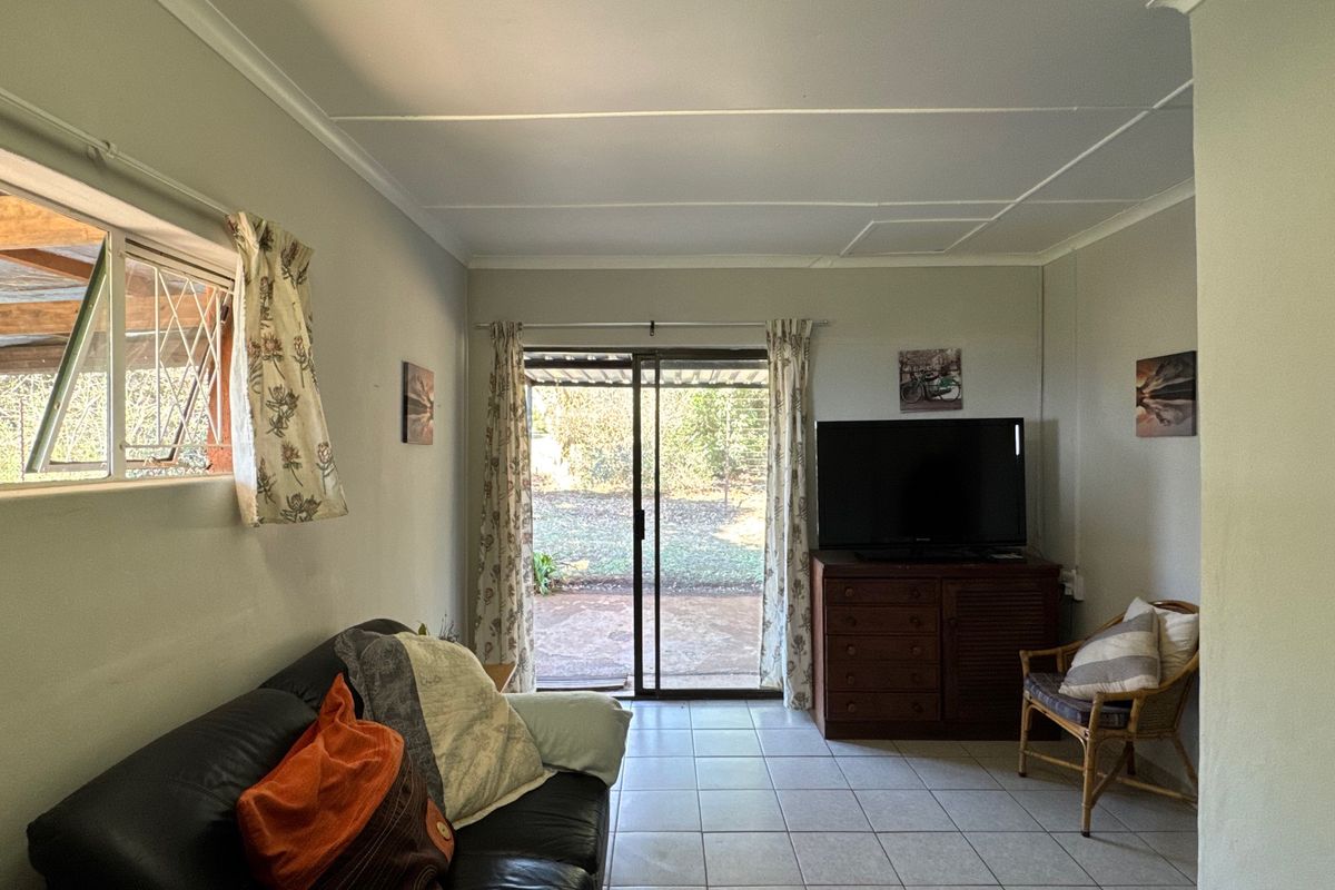 A living room featuring tiled flooring, a sliding glass door leading to the rear garden, and an awning window with security bars.