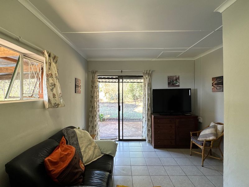 A living room featuring tiled flooring, a sliding glass door leading to the rear garden, and an awning window with security bars.