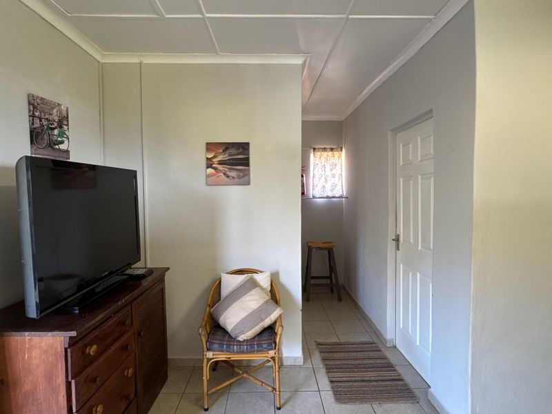 A living area featuring tiled flooring and a panelled ceiling, leading to a secondary space with a small window.
