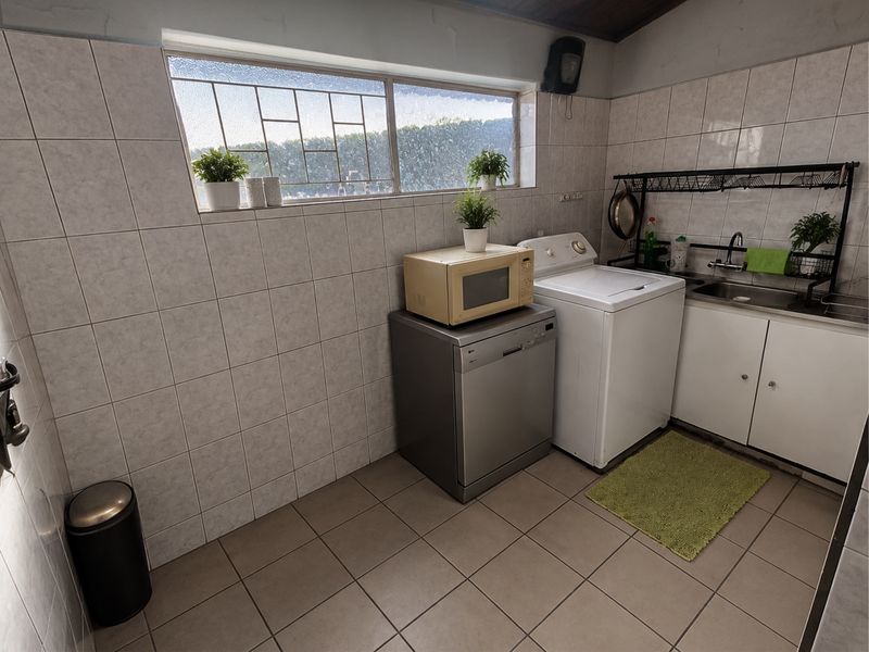 Functional laundry room featuring tiled walls and flooring, a stainless steel sink, and dedicated space for laundry appliances.