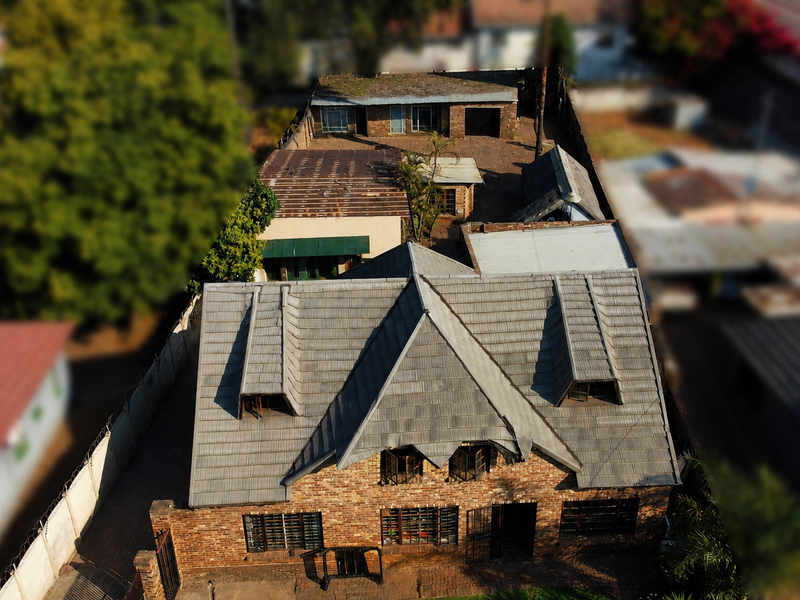 Aerial view of a brick house featuring a tiled roof with visible damage and security features, situated on a long residential plot.