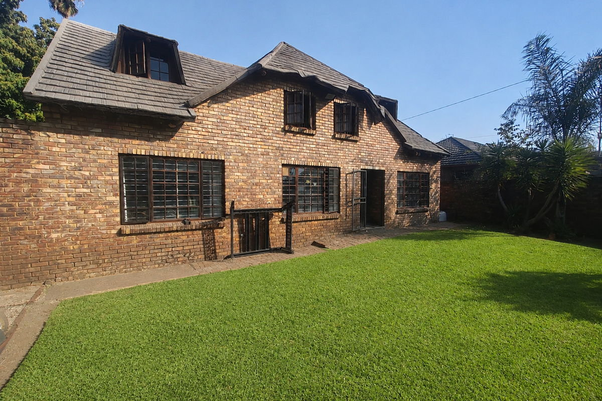 Rear view of a double-story face brick house featuring a tiled roof with dormer windows and a well-maintained lawn.