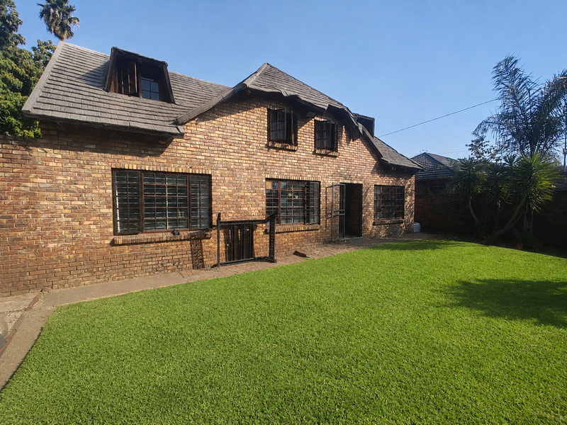 Rear view of a double-story face brick house featuring a tiled roof with dormer windows and a well-maintained lawn.