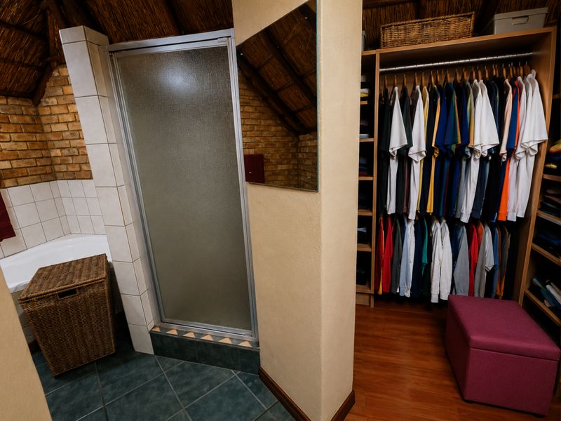 Bedroom featuring an open-plan layout with an integrated shower, corner bathtub, and built-in wardrobe storage, set under a rustic thatched roof.