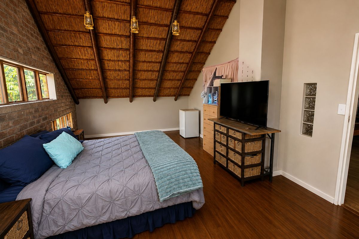 Spacious bedroom featuring a high vaulted thatched ceiling with exposed timber rafters, exposed brick wall accents, and warm laminate flooring.