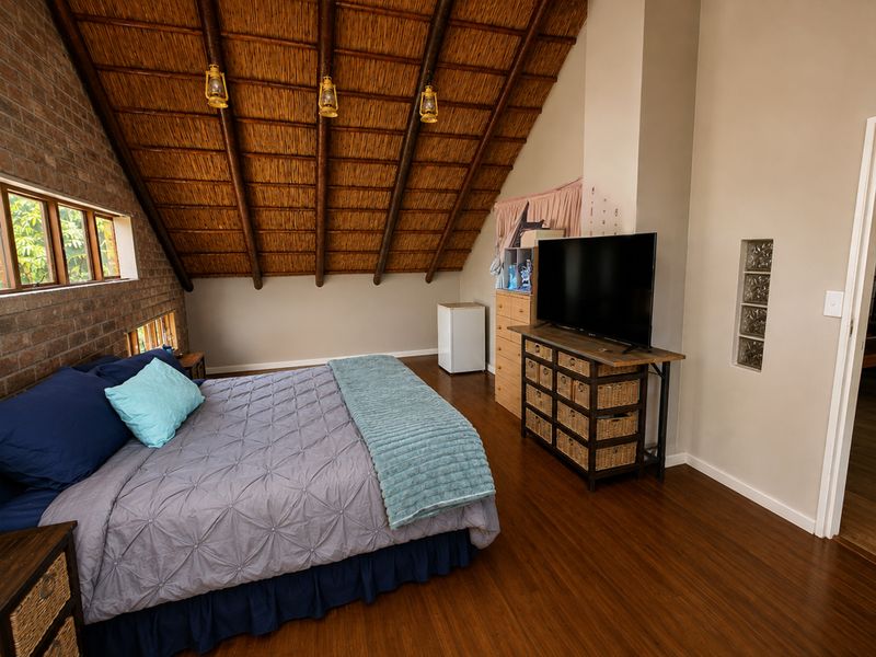 Spacious bedroom featuring a high vaulted thatched ceiling with exposed timber rafters, exposed brick wall accents, and warm laminate flooring.