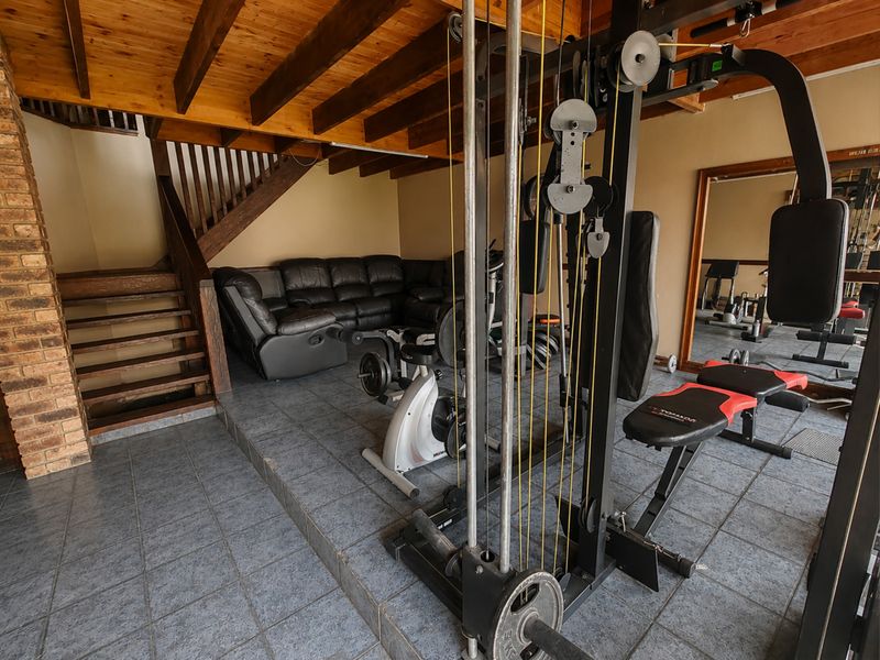 A multi-purpose gym area featuring exposed timber ceiling beams, a wooden staircase, and durable tiled flooring with a brick feature wall.