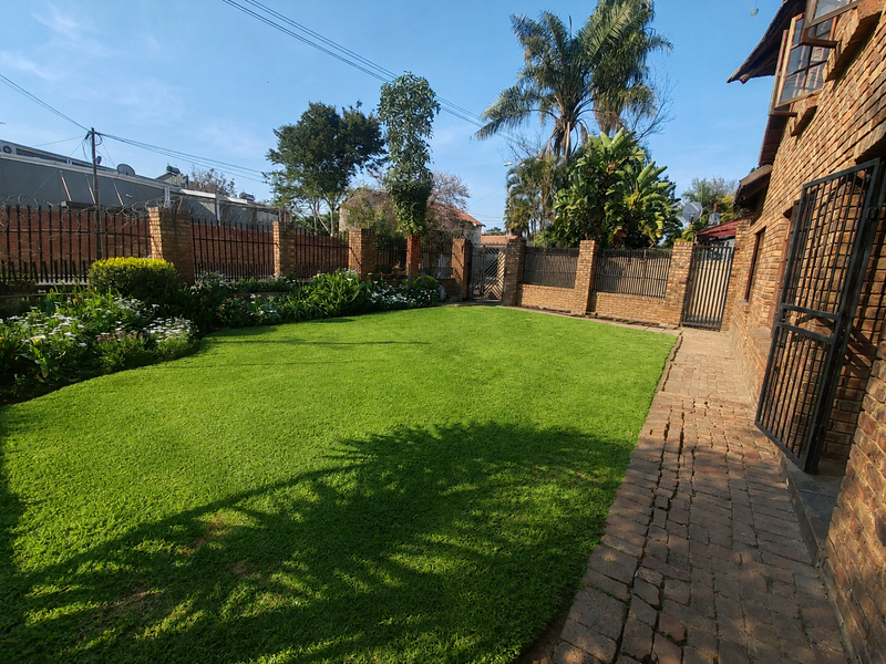 A well-maintained rear garden featuring a lush green lawn, paved walkway, and secure brick boundary walls with metal fencing.