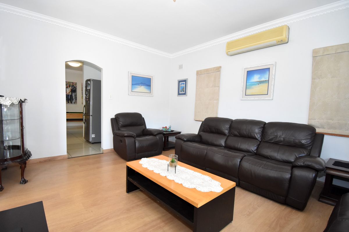 A comfortable living room featuring laminate flooring, decorative cove cornicing, and a wall-mounted split-system air conditioner.