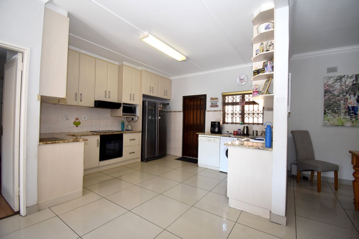 Functional kitchen featuring light-toned built-in cabinetry, granite countertops, integrated appliances, and tiled flooring with direct access to the exterior.