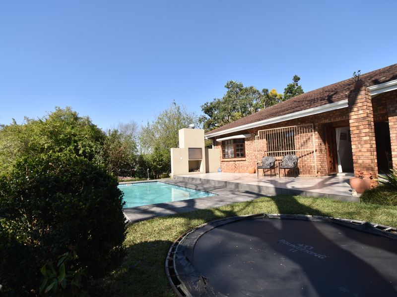 Rear exterior view featuring a swimming pool, tiled patio area, and a built-in outdoor braai against a brick house facade.
